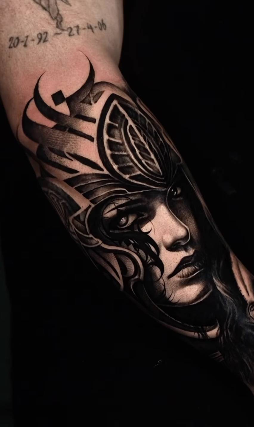 Arm tattoo featuring dates and abstract tribal design transitioning into a detailed woman's face with ornate elements